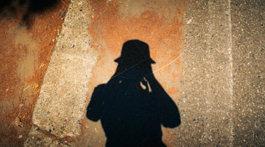 Shadow of a person in a hat on textured ground.